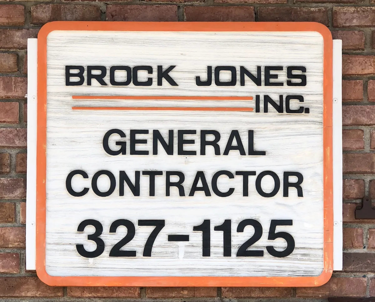 The Brock Jones, Inc. sign on the brick wall of the 14th Street office: General Contractor, 327-1125, on whitewashed wood with an orange frame